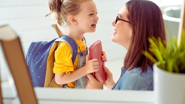 Child with a yellow shirt and blue polka-dot backpack holding a pink book, smiling at an adult in a light blue shirt, depicting a supportive moment before school. Perfect for easing back-to-school anxiety in children with autism.