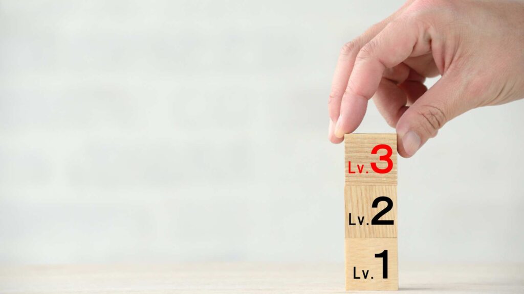 A set of wooden blocks showing levels 1, 2, and 3 being stacked by a hand, representing the range of autism levels