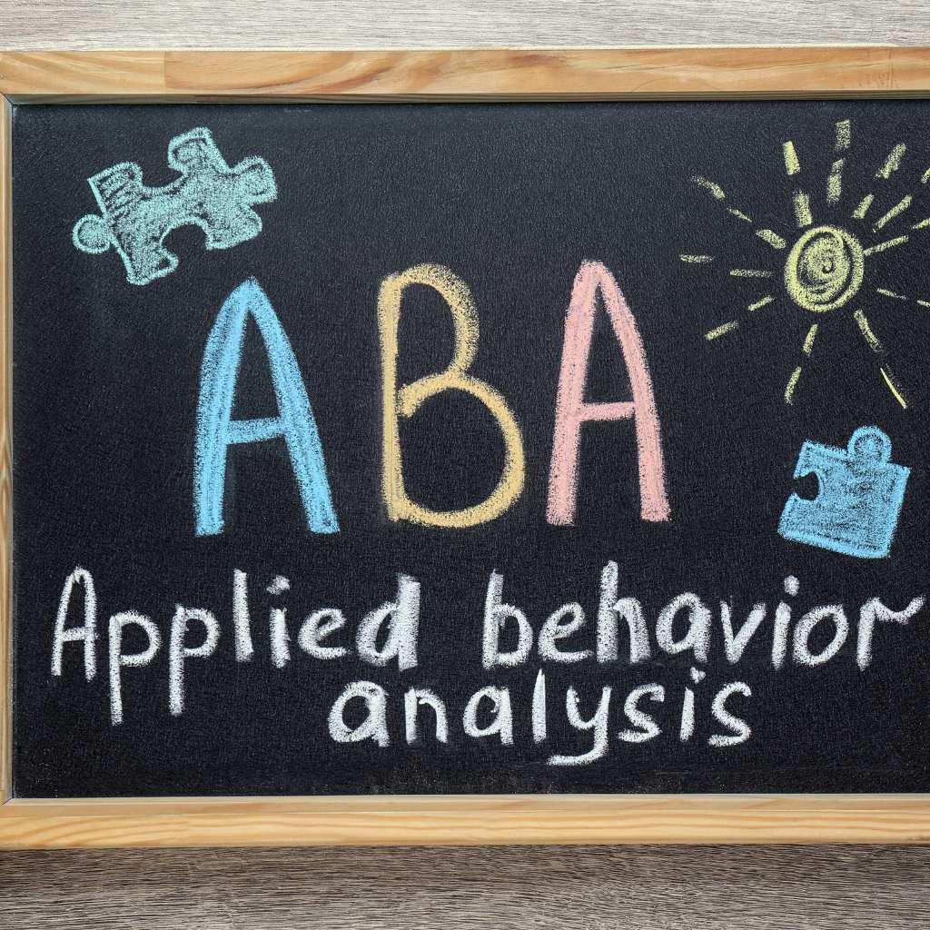 Blackboard with colorful chalk text reading 'ABA Applied Behavior Analysis' and puzzle piece drawings