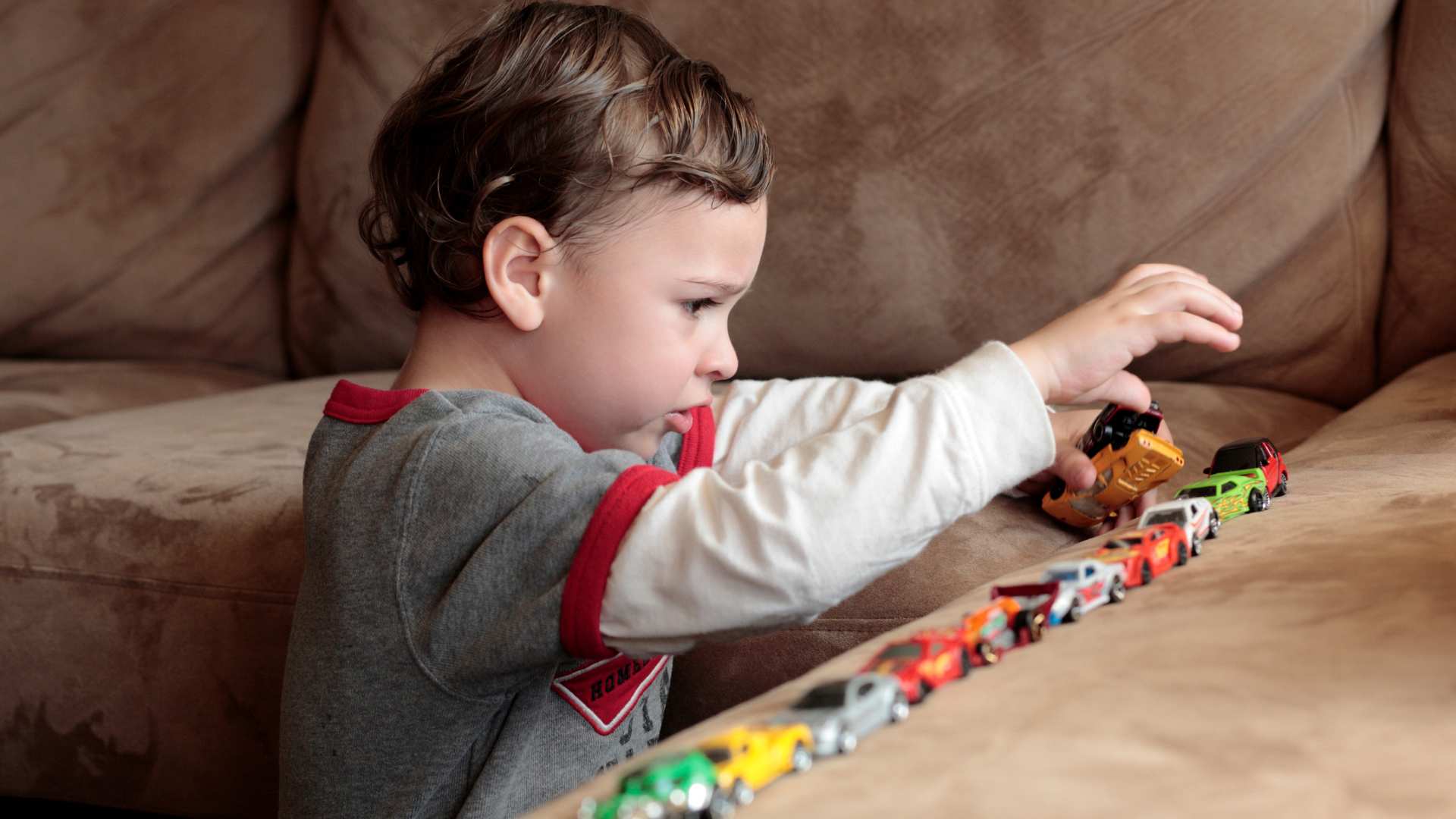 Child lining up small toy cars on a couch