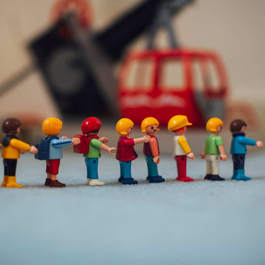 Small toy figures standing in a line with a blurry red vehicle behind them