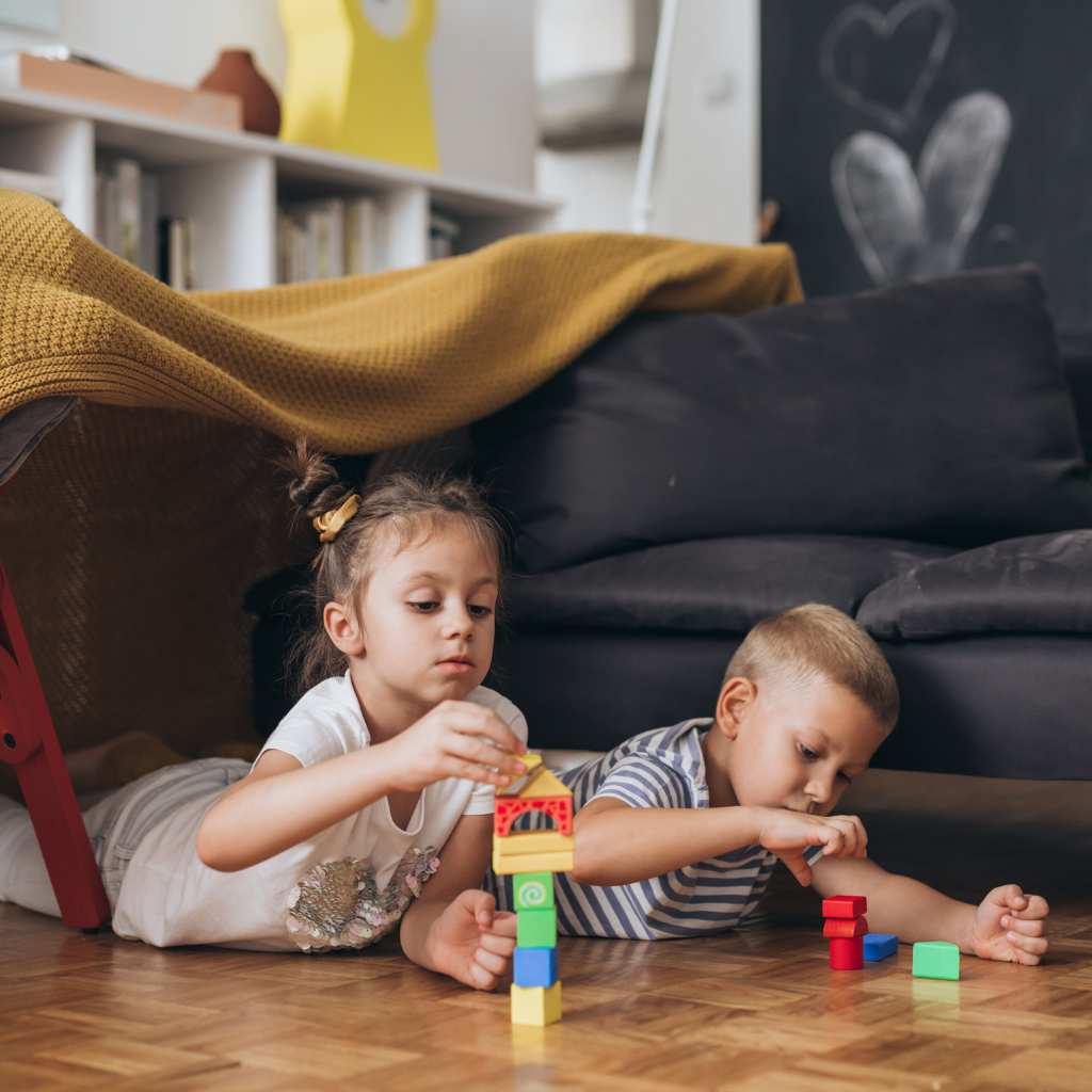 Two young children building with colorful blocks together on a living room floor, practicing social play and friendship skills