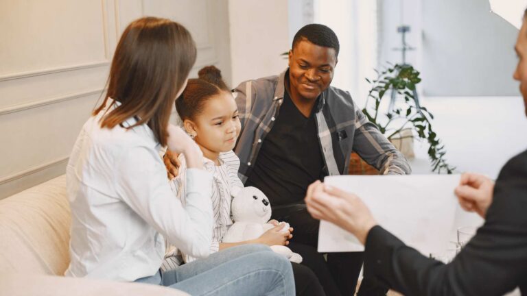 Young girl holding a stuffed animal sits with her parents on a couch while a therapist explain what is ABA therapy